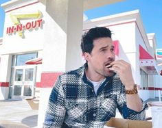 a man sitting at a table eating food in front of a fast food restaurant,