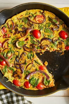 an omelet with tomatoes, onions and mushrooms in a skillet on a table