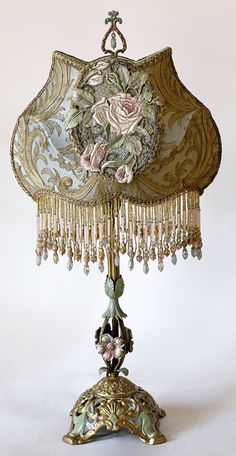 an ornate lamp with flowers and beads hanging from it's base on a white background