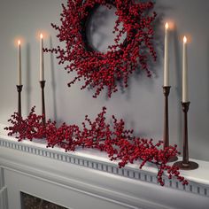 a wreath on top of a mantle with candles in front of it and red berries all over the mantle