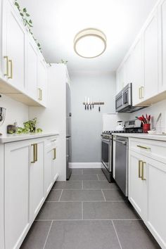 a long narrow kitchen with white cabinets and stainless steel appliances on the wall, along with gray tile flooring