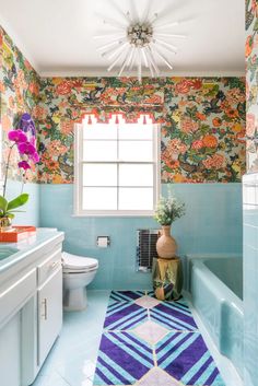 a bathroom with blue tile and floral wallpaper on the walls, along with a rug that matches the bathtub