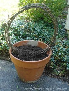 a planter filled with dirt sitting on top of a cement floor next to bushes