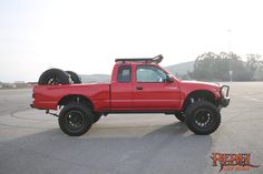 a red pick up truck parked in a parking lot with two large tires on the back