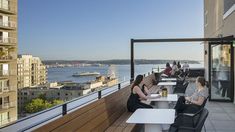 people are sitting at tables on the roof of a building with water in the background