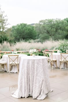 the table is set up with white linens and flowers on it for an outdoor wedding reception