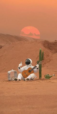 an astronaut sitting on the ground next to a cactus and holding a guitar in his hand