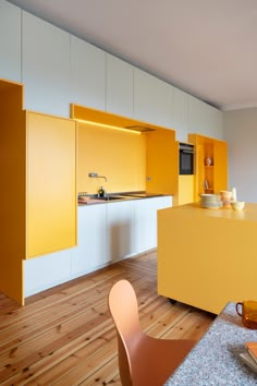 a kitchen with yellow cabinets and wooden flooring next to a dining room table that has two plates on it