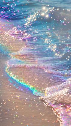 an ocean wave with colorful bubbles coming out of it's water and the beach is covered in sand