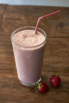 a smoothie in a glass with strawberries next to it on a wooden table