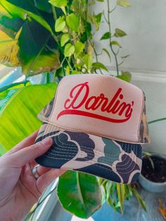 Show of your style in our Darlin' Country Western trucker hat. - Features the phrase "Darlin' " across the front in a red ink on a tan/camo hat- Come with a removable small brown pin attached to each hat - Individually heat pressed onto each hat - 5 Panel, Mesh Back with Snap Back *due to screens & filters colors may vary slightly to photos* Western Trucker Hats, Camo Hat, Camo Hats, Red Ink, Country Western, Snap Back, Snap Backs, Trucker Hats, Trucker Hat