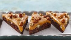 four pieces of brownie with caramel toppings sitting on a baking sheet next to a candle