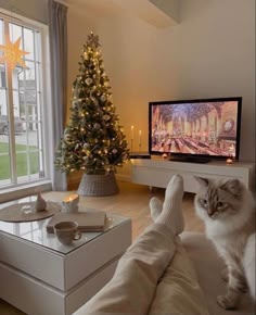 a cat sitting on the arm of a couch in front of a christmas tree and television