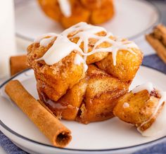 cinnamon rolls with icing on a plate next to cinnamon sticks and a glass of milk