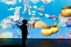 a little boy standing in front of a big screen with fish and jellyfish on it