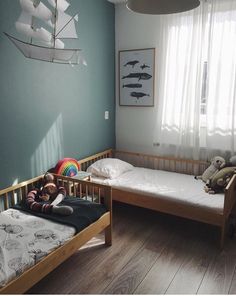 two small beds with stuffed animals on them in a room that has blue walls and wooden floors