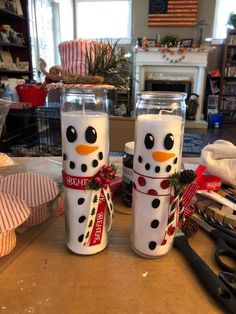 two snowman candles are sitting on a table with scissors and other holiday decorations in the background