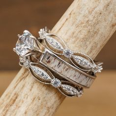 two wedding rings on top of each other sitting on a piece of driftwood in front of a wooden background