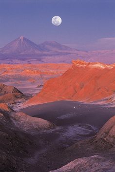 the moon shines brightly in the sky over mountains and desert land, with snow capped peaks