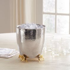 a silver bowl with ice in it sitting on a table next to glasses and napkins