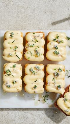 there are many small pieces of bread with white frosting on them and sprinkled with herbs