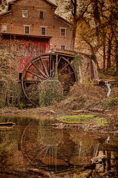 an old water wheel sits in front of a red barn with a reflection on the water