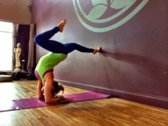 a woman doing a handstand on a yoga mat in front of a wall