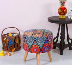 two small stools with colorful designs on them next to a round table and basket