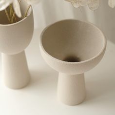 two white vases with flowers in them on a table next to each other,