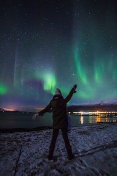 a man standing on top of a snow covered ground under the stars and aurora lights