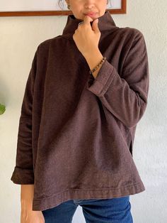 a woman standing in front of a wall with her hand on her chin and looking at the camera