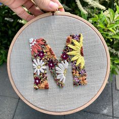 a person holding up a cross stitch letter m