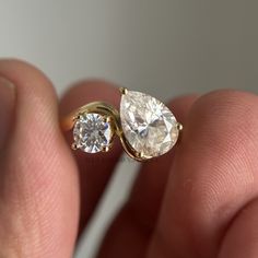 a close up of a person's hand holding an engagement ring with two pear shaped diamonds