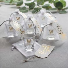 four personalized shot glasses and tags on a table with greenery in the background