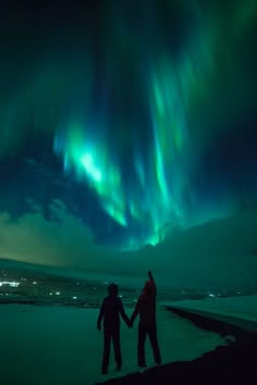 two people holding hands in front of an aurora bore over the ocean at night time