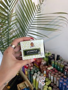 a person holding up a business card in front of a large amount of bottles and palm leaves