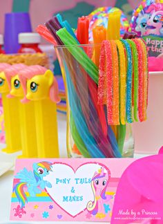 there are many colorful plastic toys in the vases and on the table is a sign that says, my little pony party food ideas