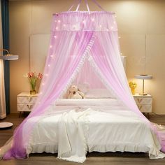 a pink canopy bed with white sheets and lights on the headboard is in a bedroom