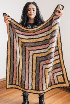 a woman holding up a multicolored crocheted blanket in front of her face