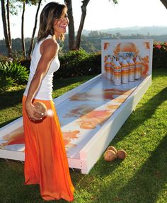 a woman in an orange skirt standing next to a giant bowling game on the grass