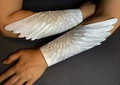 two hands with white wings on them are holding onto each other's arm sleeves