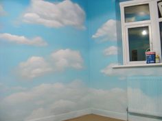 there is a room with clouds painted on the wall and window in the corner,