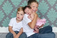 three children sitting on the floor with their arms around each other