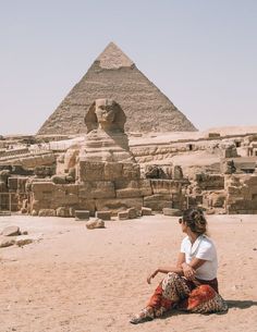 a woman sitting on the ground in front of a pyramid