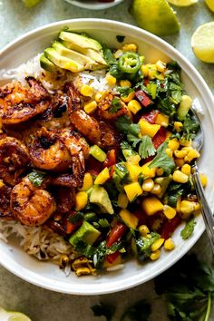 a white plate topped with shrimp and rice next to lime wedges on a table