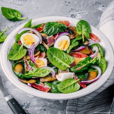 a white bowl filled with spinach, hard boiled eggs and red onions on top