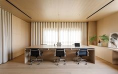 an office with two desks and chairs in front of a window that has vertical blinds