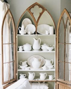 an old china cabinet is filled with white dishes and cups on it's shelves