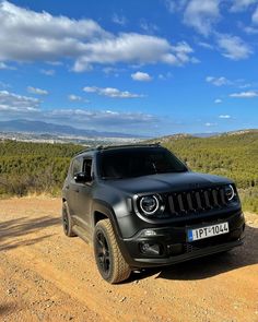 the jeep is parked on the dirt road near some trees and hills in the distance