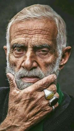 an old man with white hair and greying is posing for the camera, his hand resting on his chin